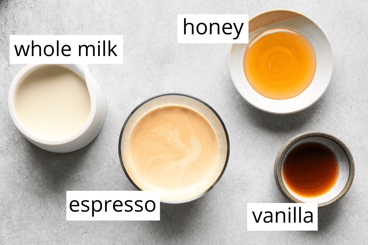 overhead photo of the ingredients in this vanilla latte recipe all in bowls and labeled including honey, whole milk, brewed espresso and vanilla
