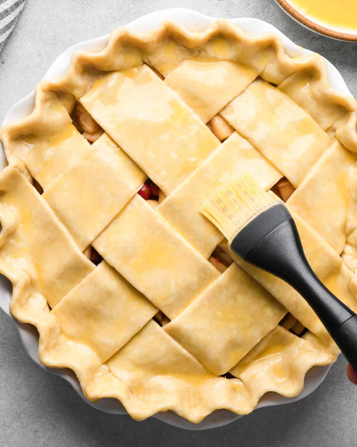 making cranberry and apple pie - egg wash being brushed over the crust with a black and clear silicone pastry brush