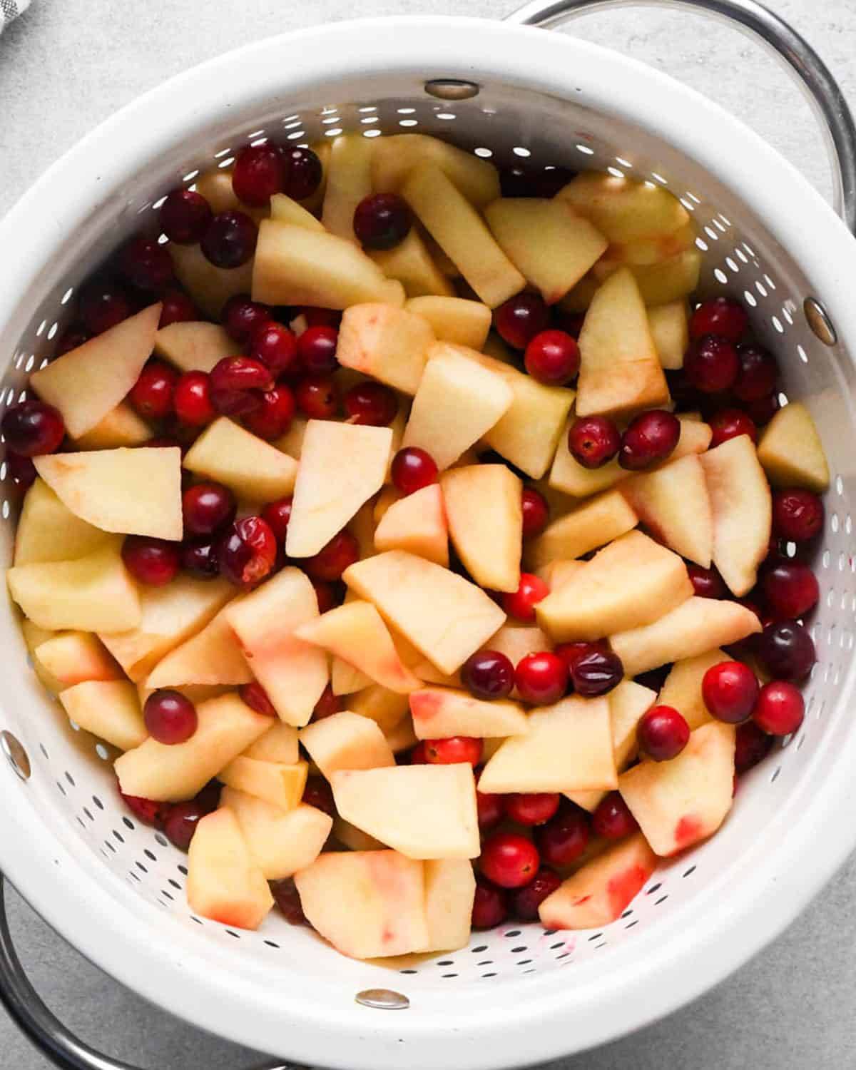 making cranberry and apple pie - peeled, cored and sliced apples and cranberries in a white colander after being microwaved for 3 minutes