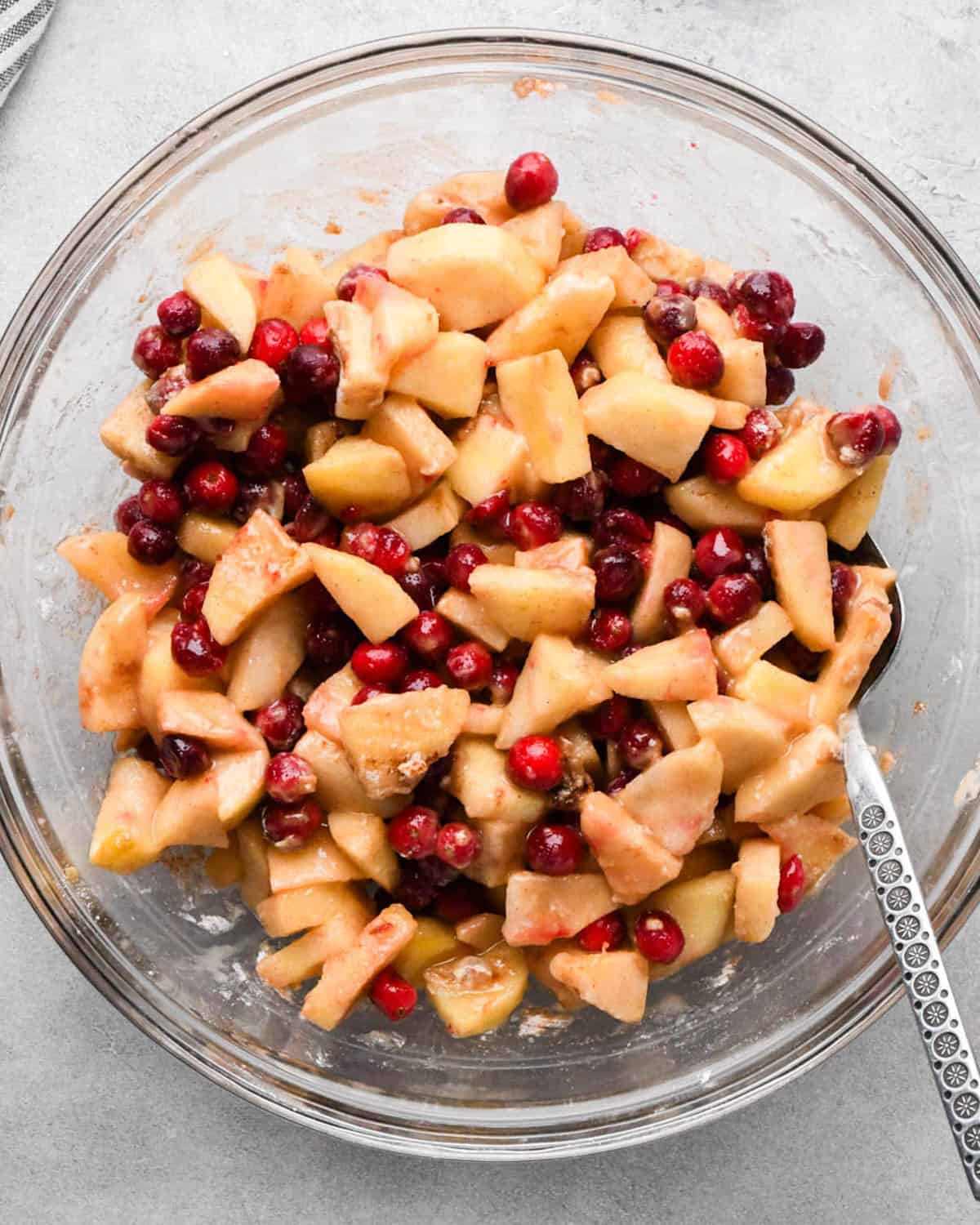 making cranberry and apple pie - filling in a glass bowl after mixing all the ingredients together with a metal spoon