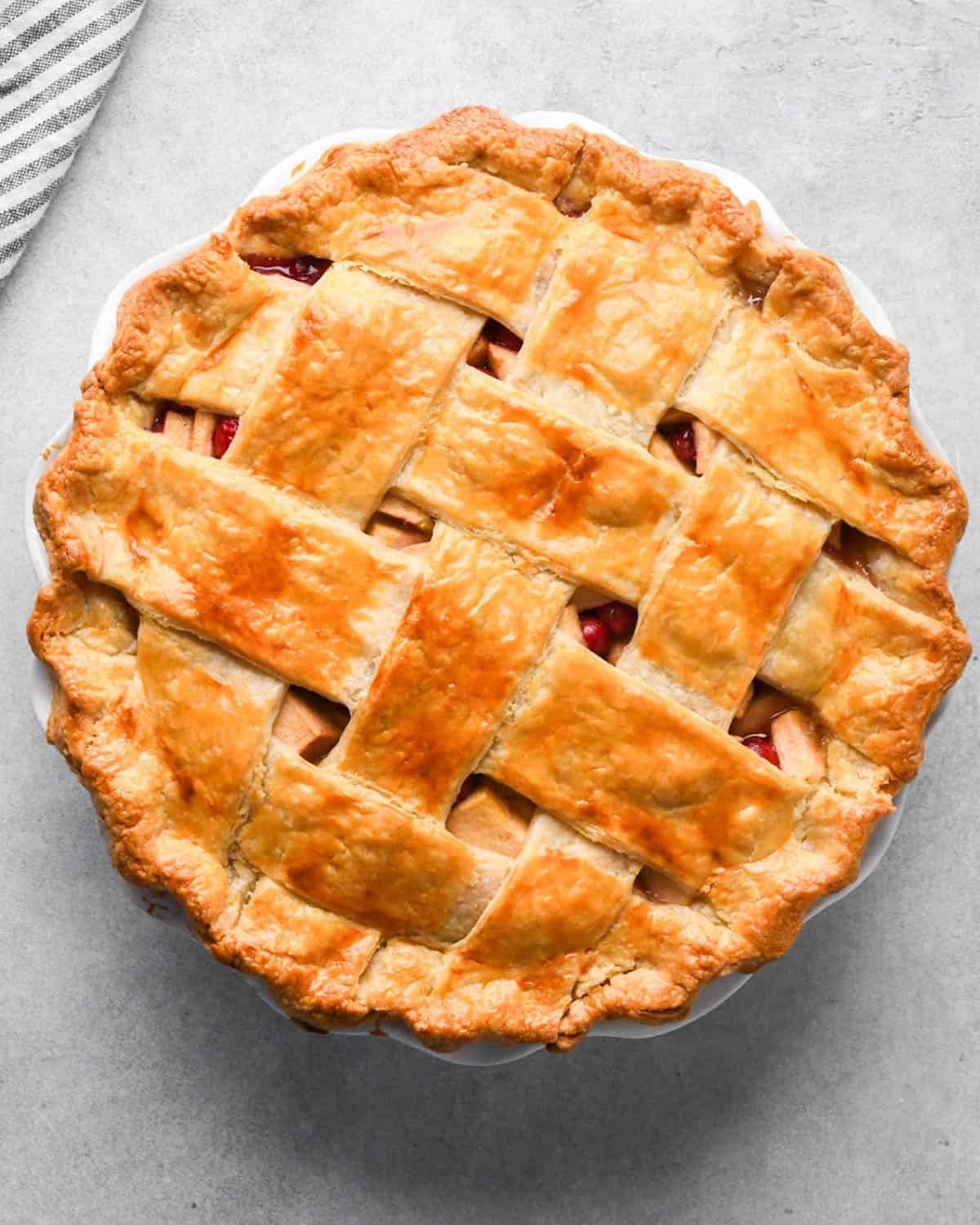 baked apple cranberry pie with a lattice crust in a white pie dish