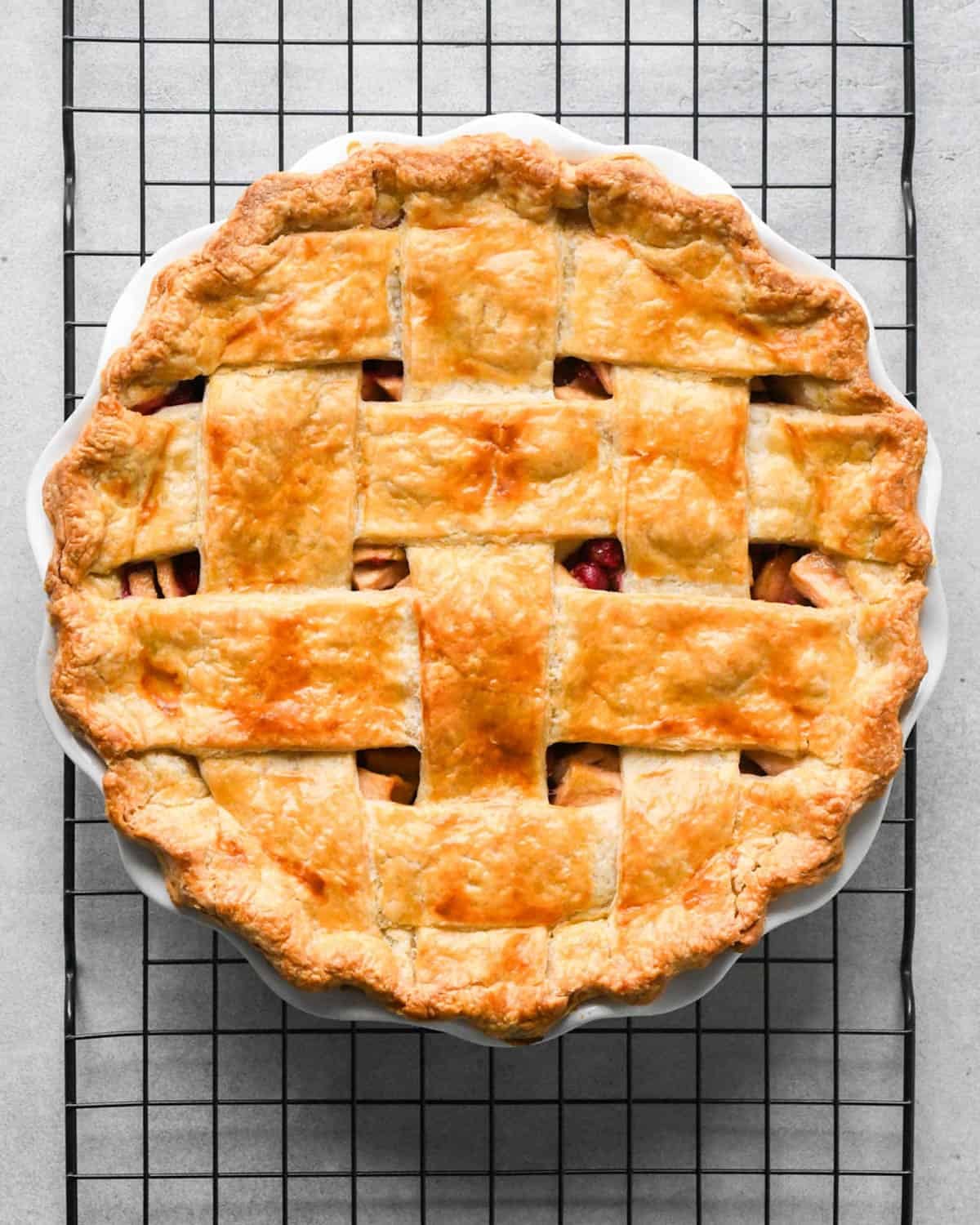 apple cranberry pie with a lattice crust in a white pie dish on a metal cooing rack