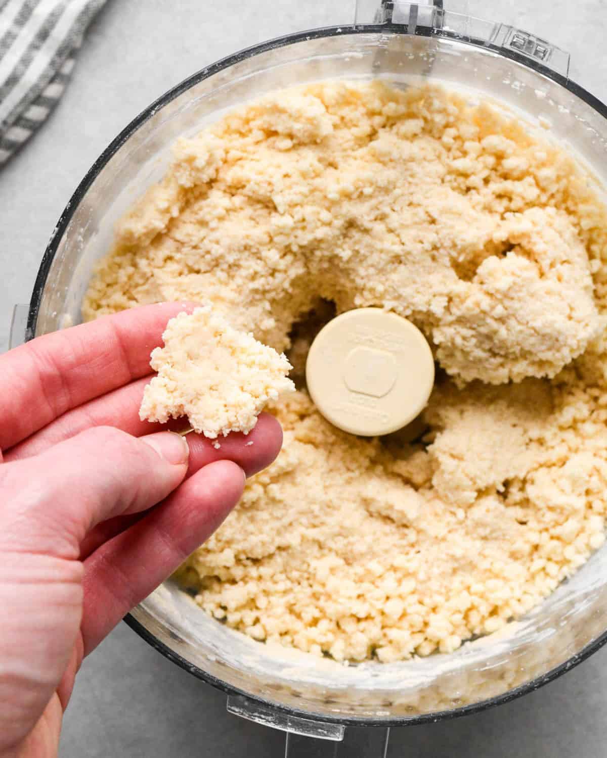 making apple cranberry pie crust - a hand pinching a piece of pie dough over the food processor showing it's done