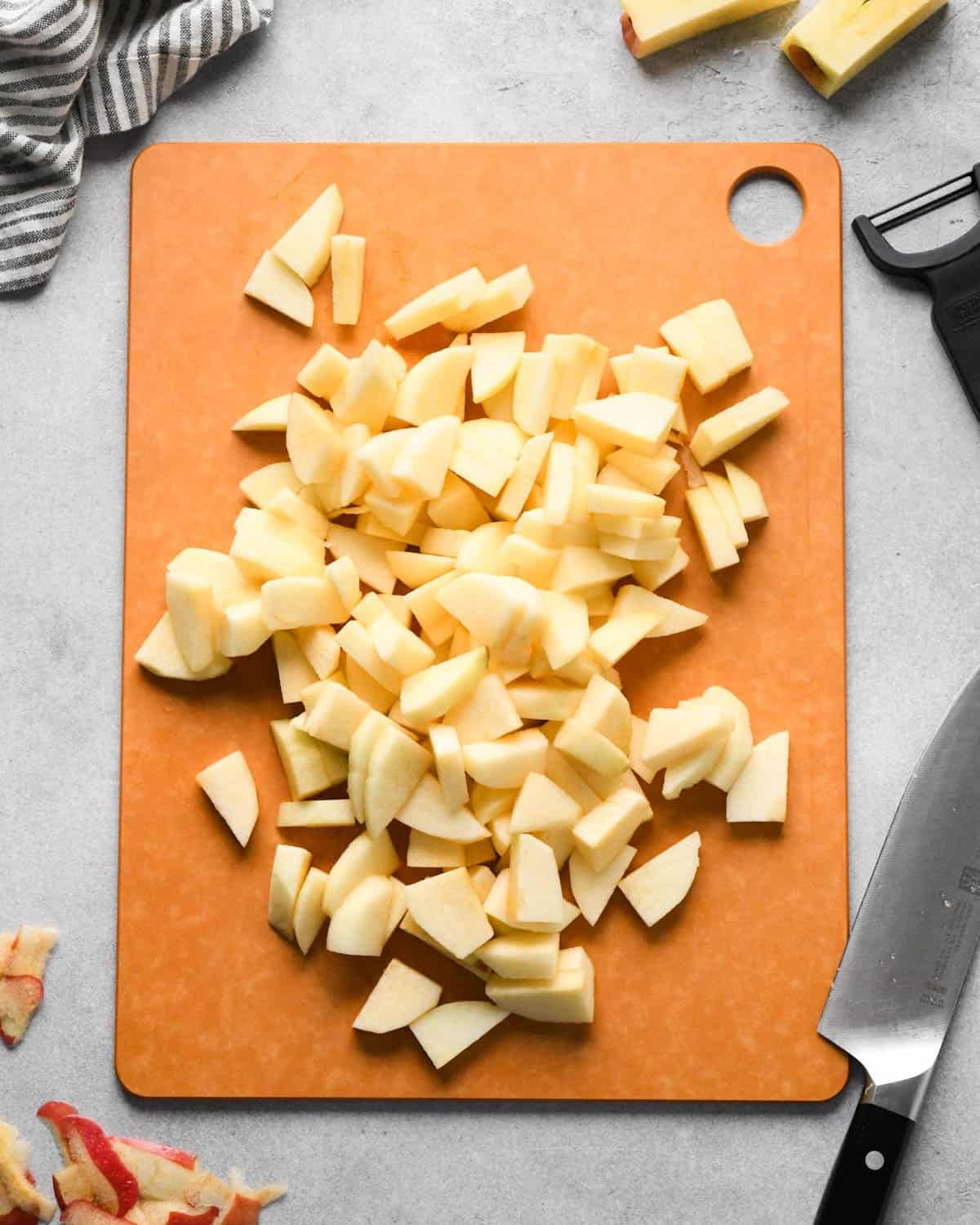 making cranberry and apple pie - peeled, cored and sliced apples on a brown cutting board