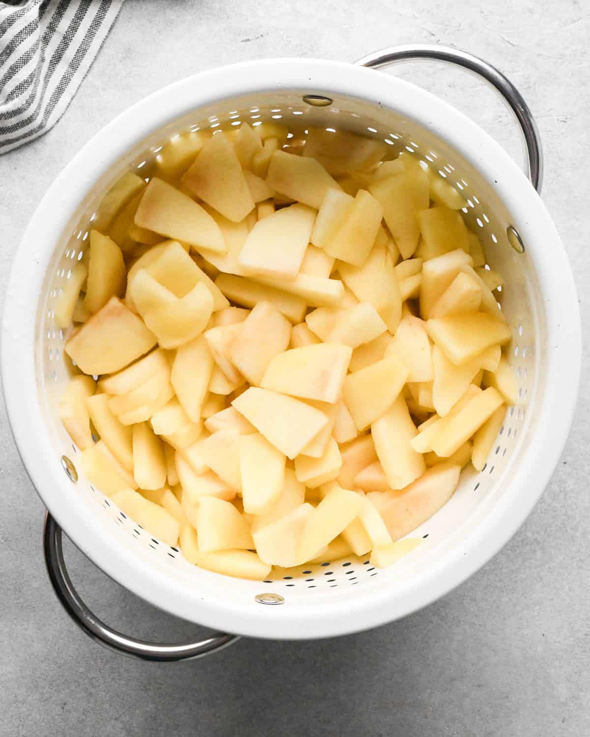 making caramel apple pie filling - peeled and sliced apples in a white colander after microwaving so the excess water can drain out