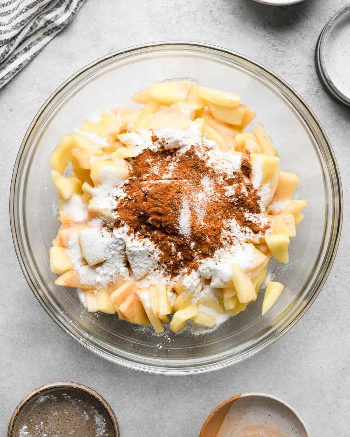 making caramel apple pie filling - apples in a glass bowl with flour, sugar, cinnamon and nutmeg before mixing
