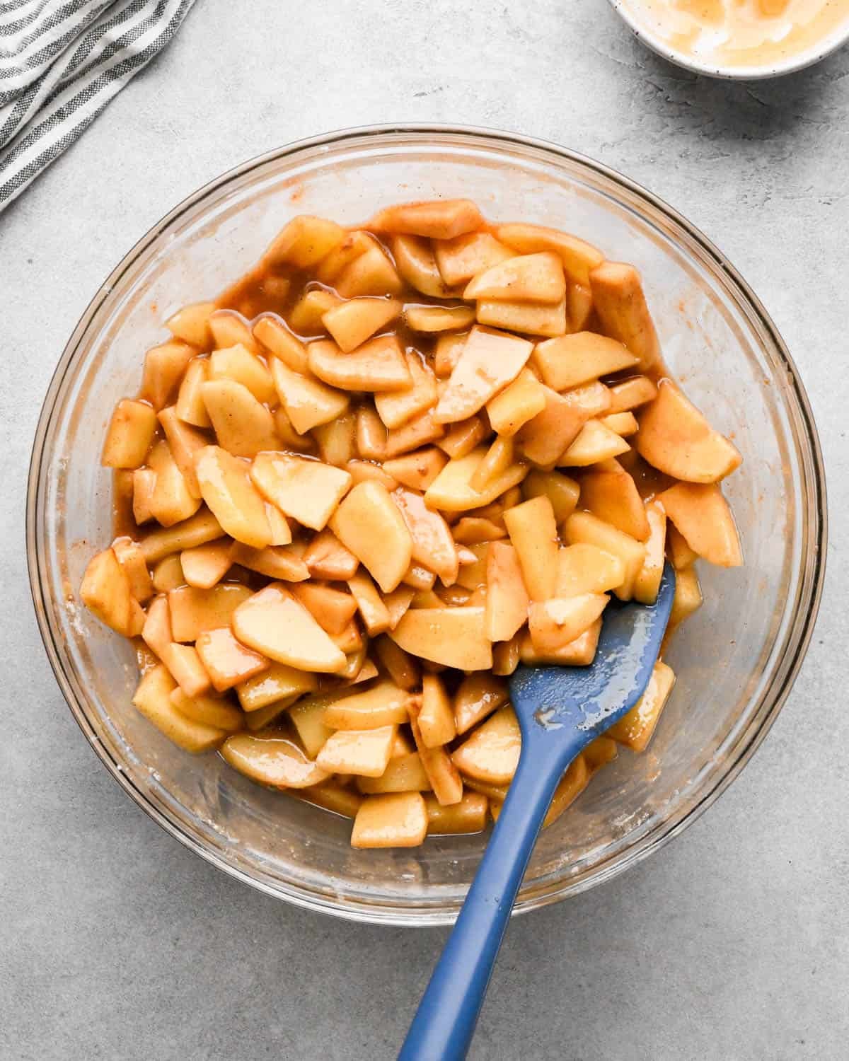 final caramel apple pie recipe filling in a glass mixing bowl with a blue spatula