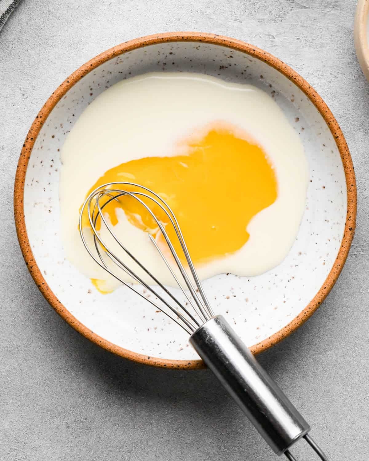 making caramel apple pie - egg yolk and cream in a small ceramic bowl with a metal whisk before mixing