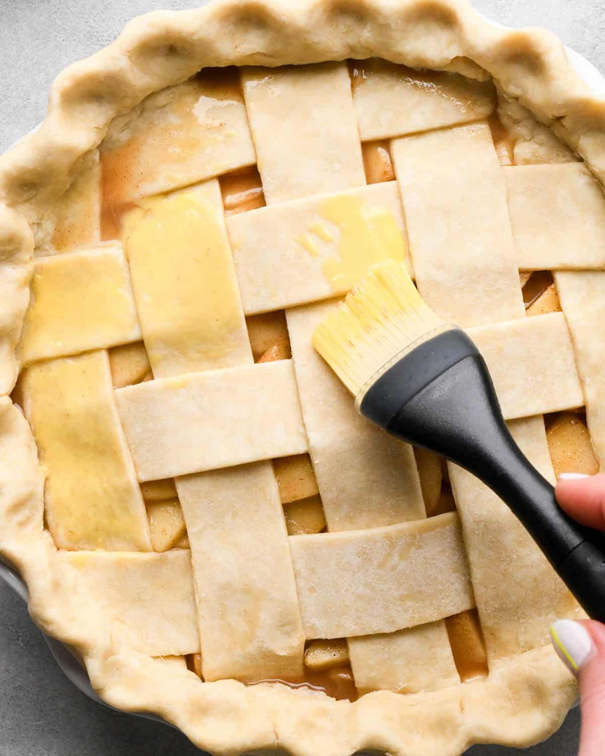 making caramel apple pie - egg wash being brushed on top of a caramel apple pie with a lattice crust with a silicone pastry b rush