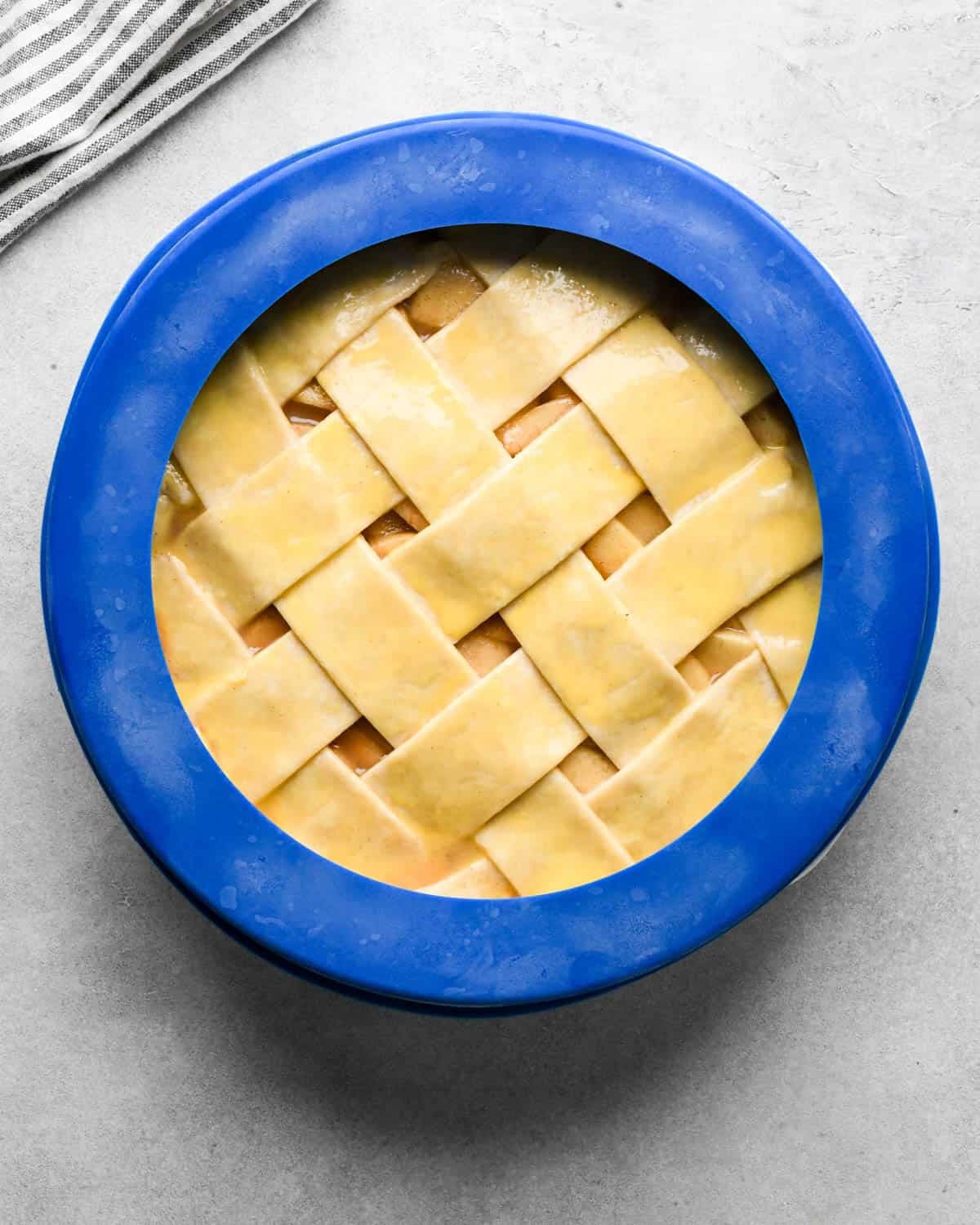 assembled caramel apple pie in a pie dish with a blue pie crust shield around the edge before baking