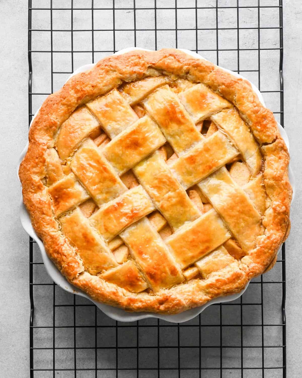 caramel apple pie with a lattice crust in a white pie dish on a black metal cooling rack after baking
