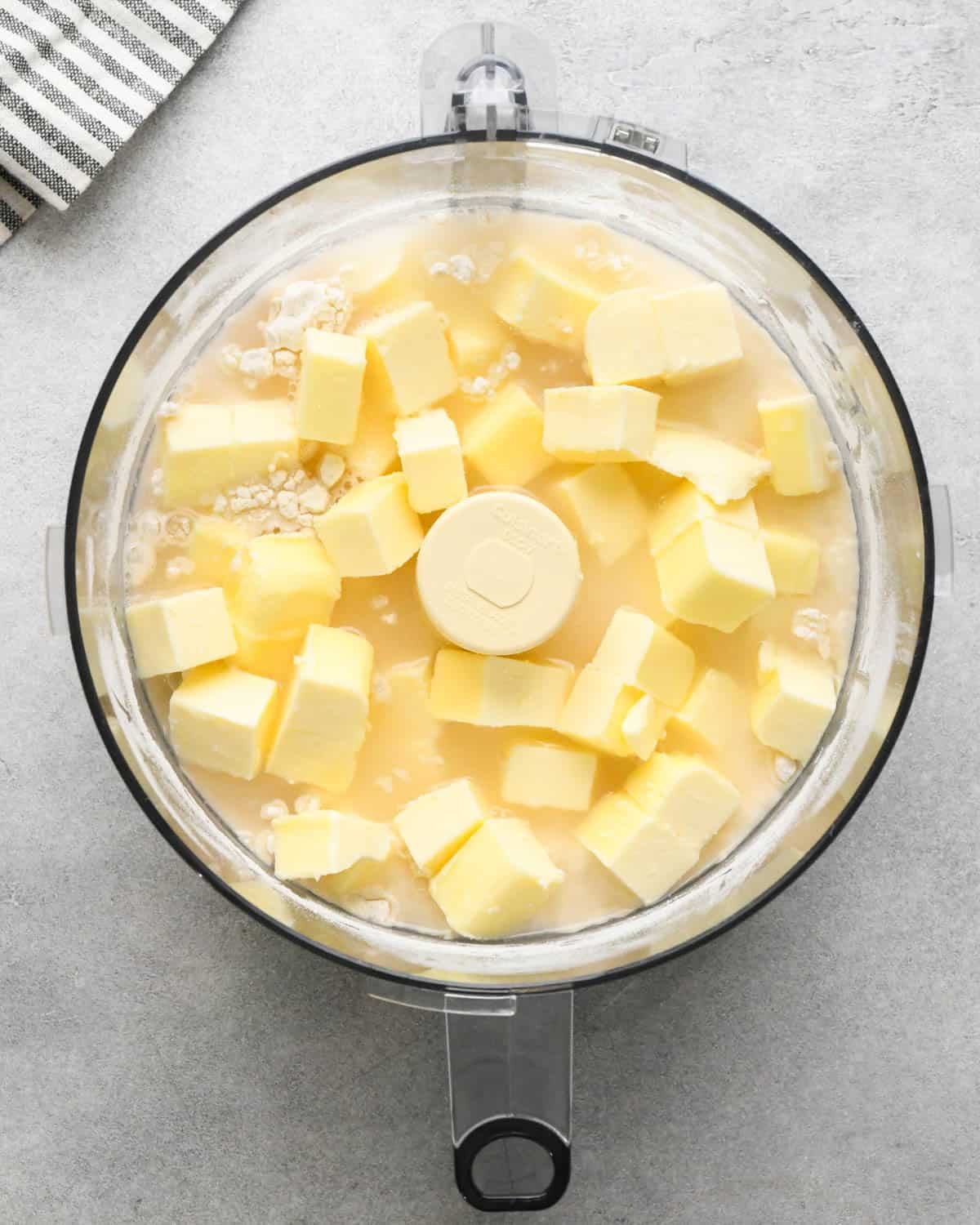 making crust for caramel apple pie - butter and water added to the dry ingredient sin a food processor fitted with the S blade before mixing