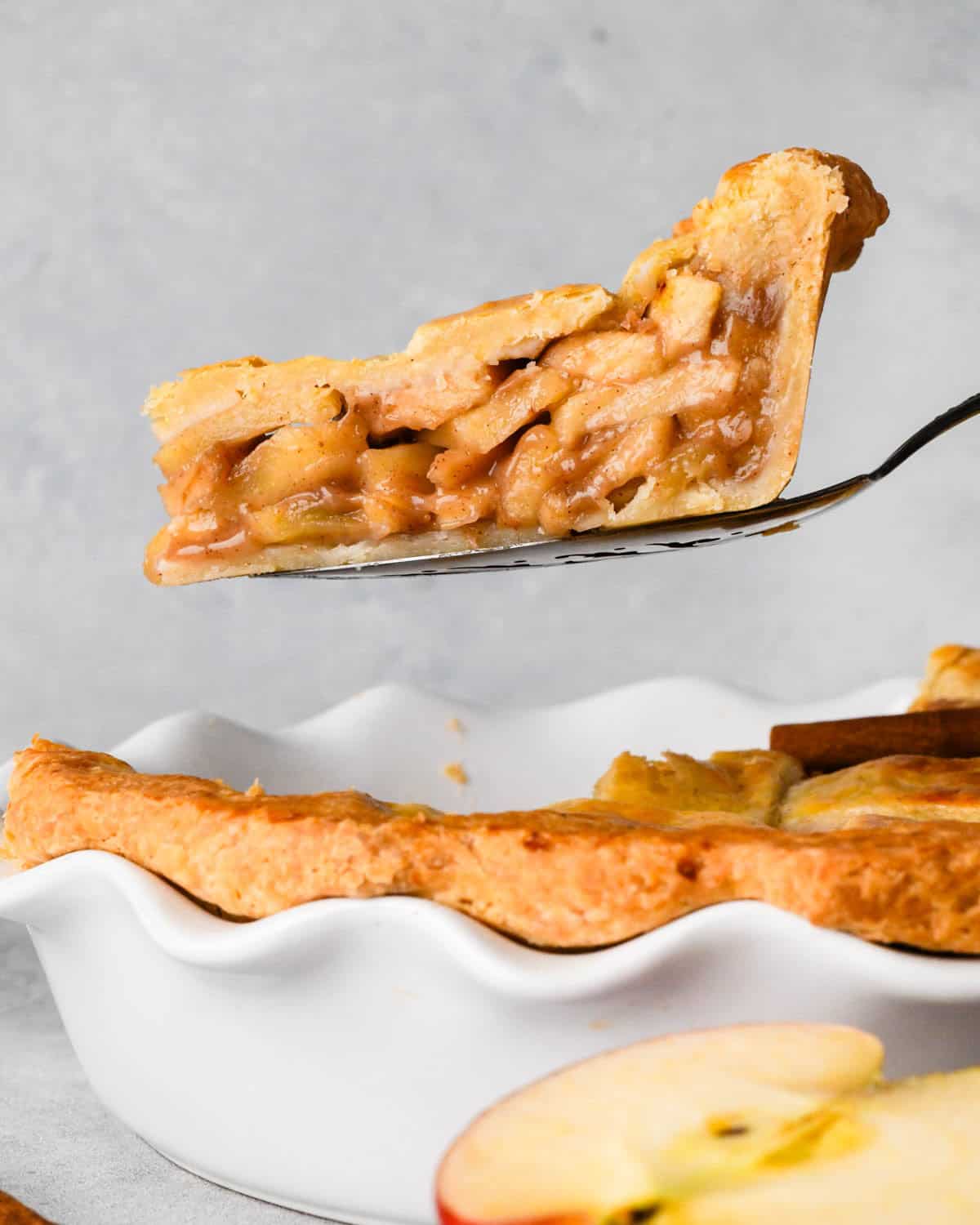 a piece of caramel apple pie being lifted out of the pie dish with a pie server so the thick caramel apple pie filling is visible