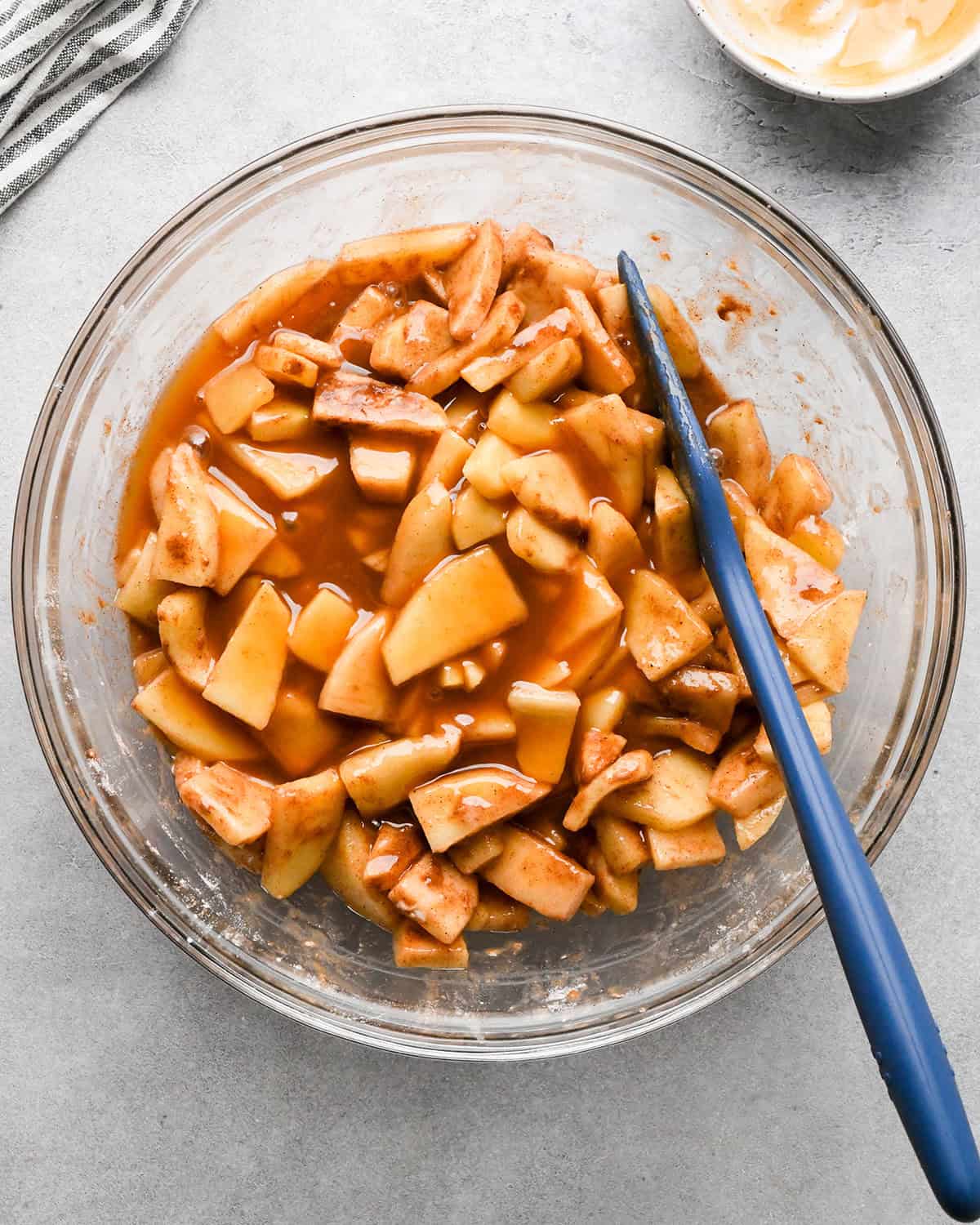 making caramel apple pie filling - caramel added to the apple mixture in a glass mixing bowl with a blue spatula before mixing