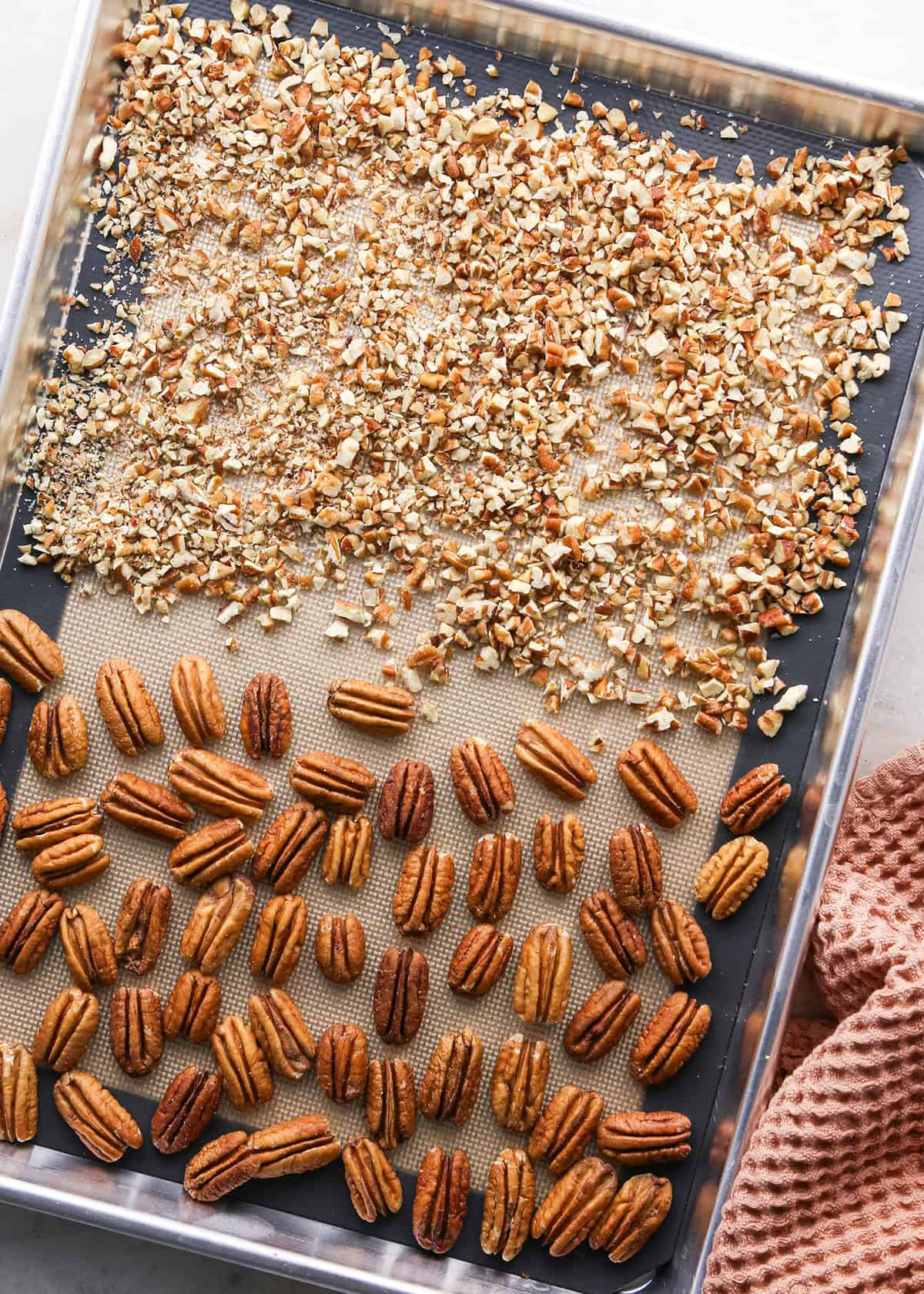 how to make pecan pie without corn syrup - chopped pecans and pecan halves on a large silver baking sheet lined with a silicone baking mat
