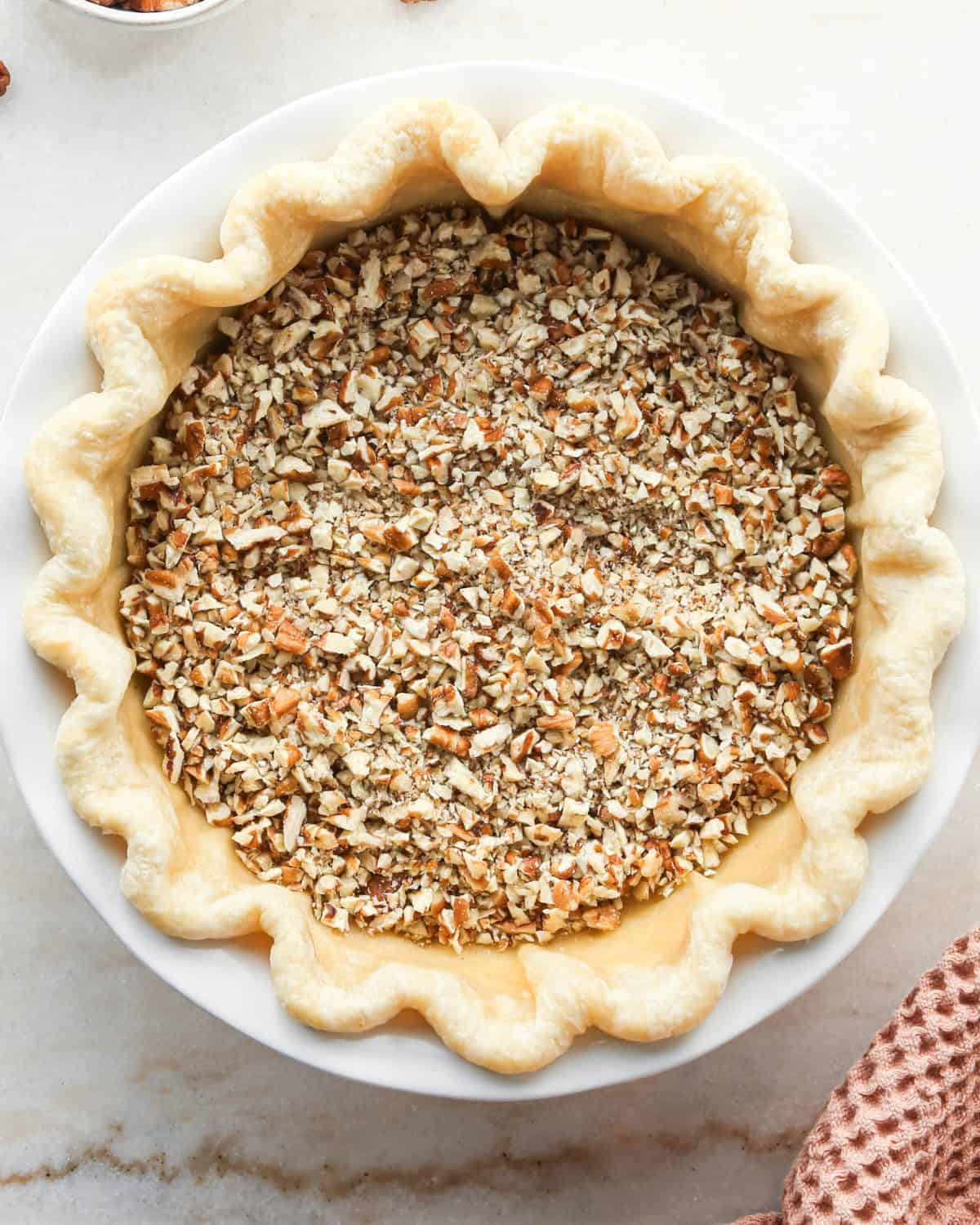 how to make pecan pie without corn syrup - chopped pecans in the bottom of the partially baked pie crust in a white ceramic baking dish