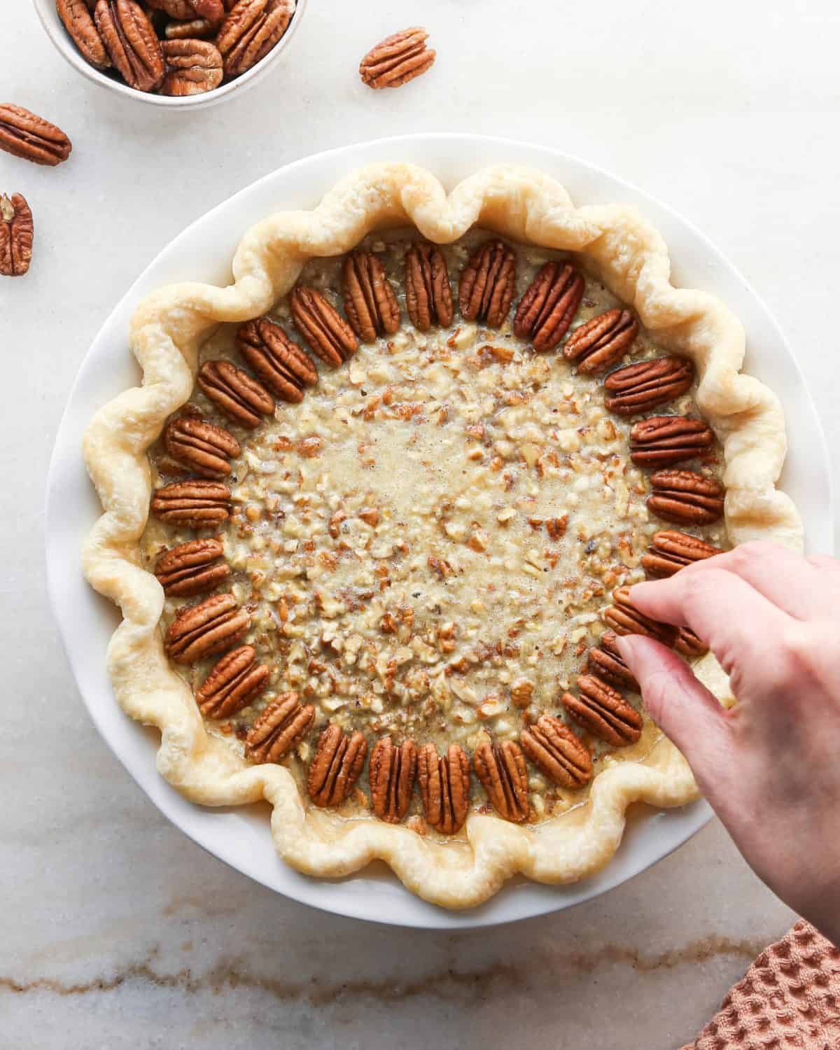 how to make pecan pie without corn syrup - a hand arranging whole pecans on top of the filling in concentric circles