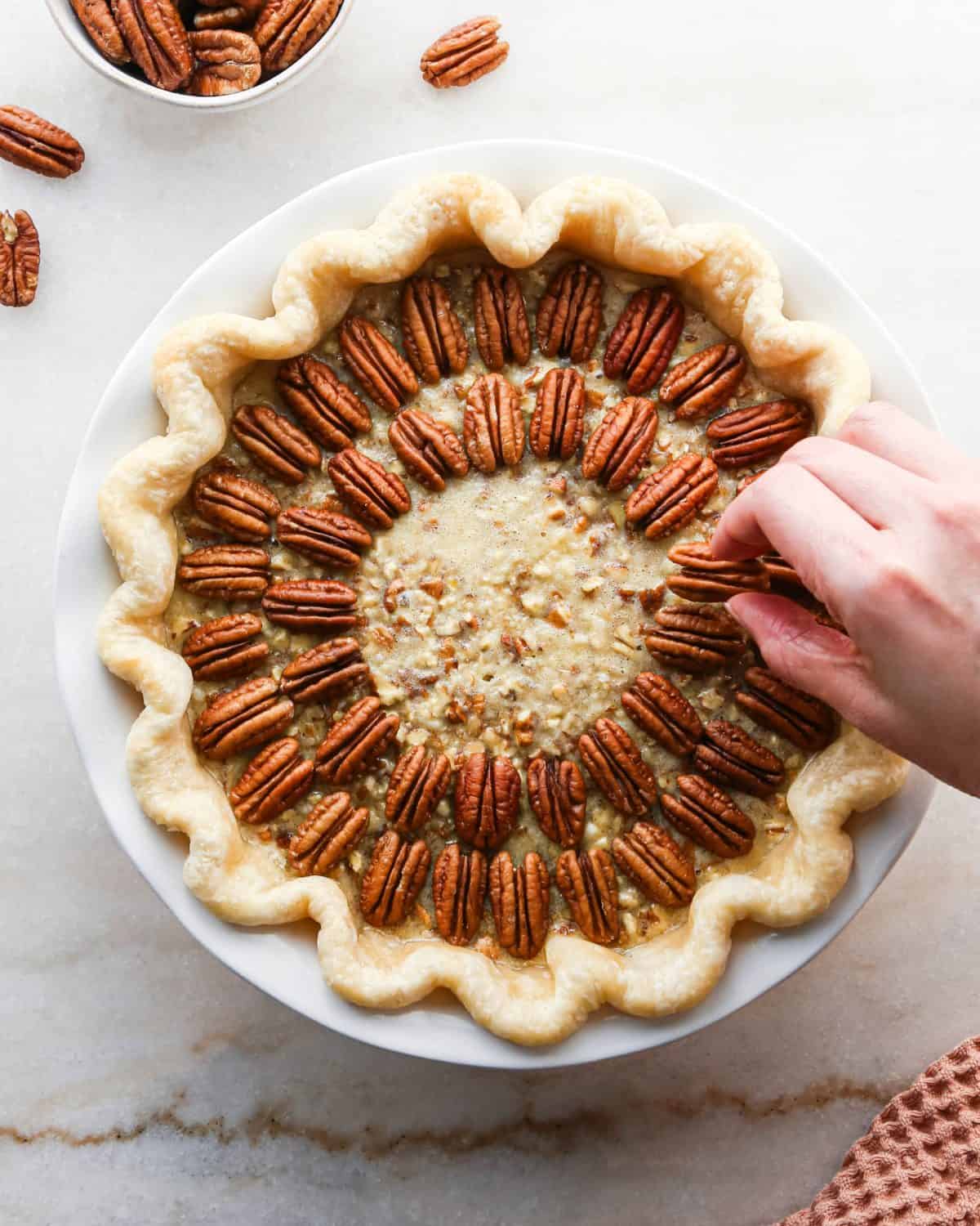 how to make pecan pie without corn syrup - a hand arranging whole pecans on top of the filling in concentric circles