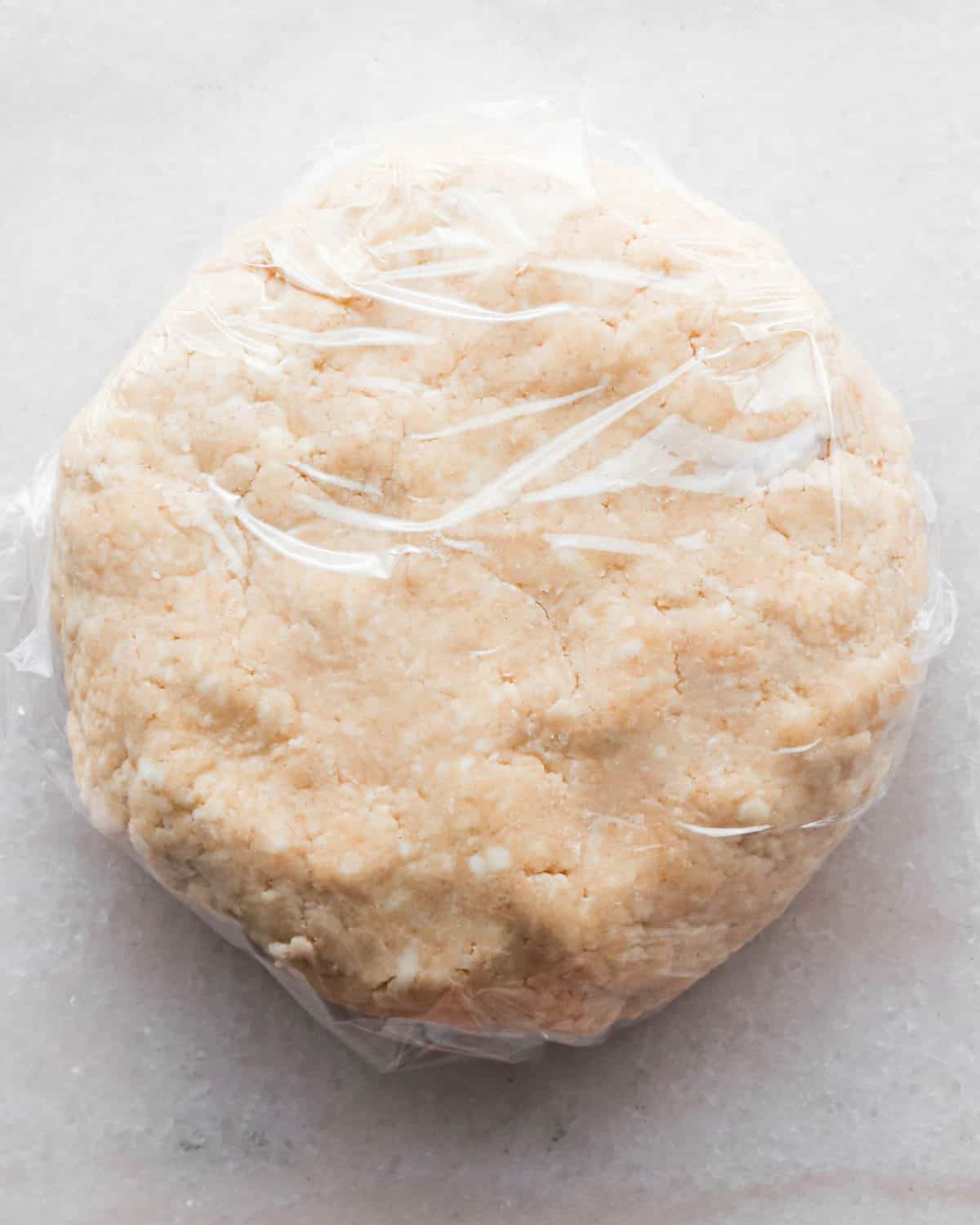 how to make pecan pie without corn syrup - pecan pie crust formed into a round disc wrapped in plastic wrap on a marble surface