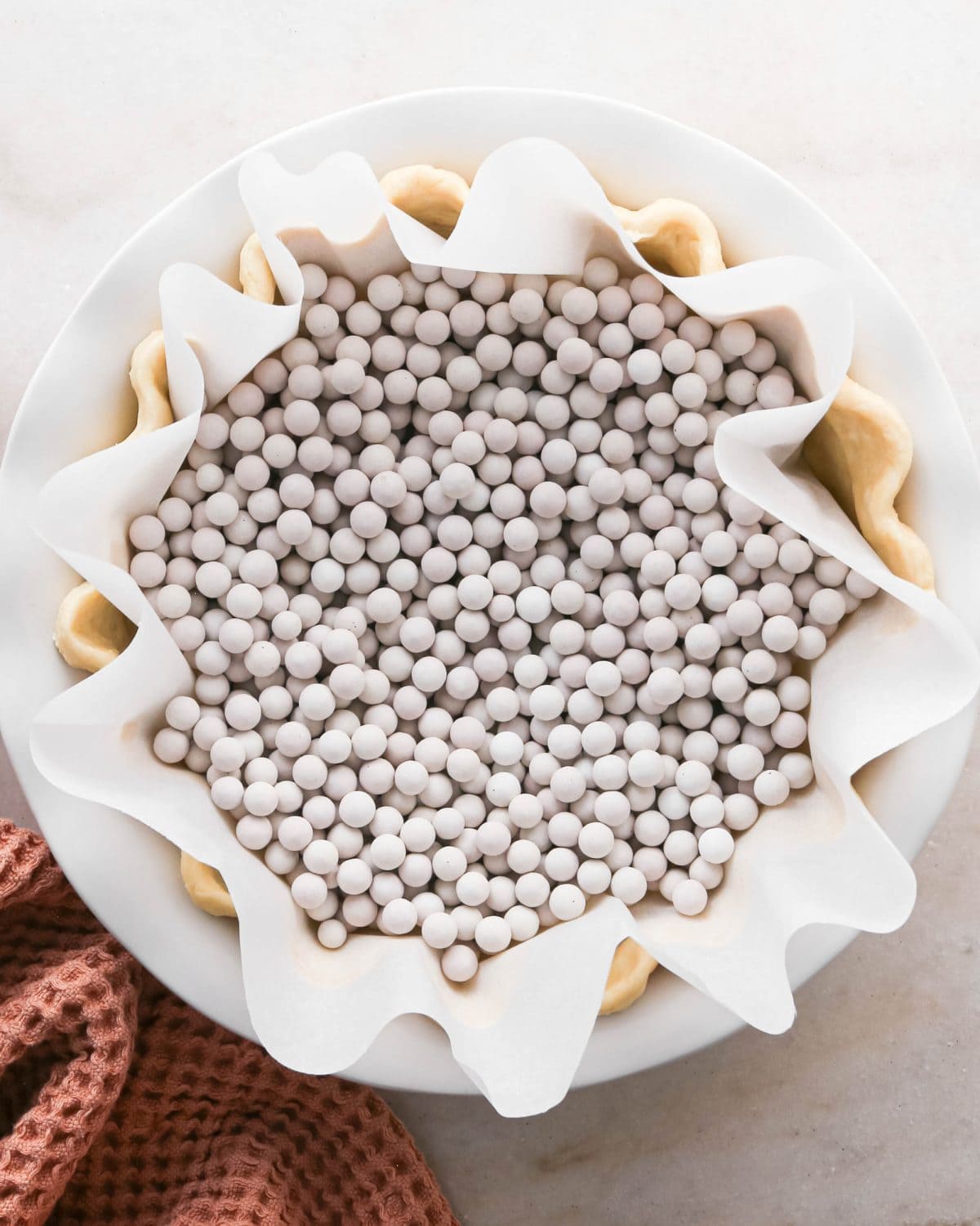 how to make pecan pie without corn syrup - pecan pie crust in the bottom of a white ceramic pie dish with a fluted edge lined with parchment paper and filled with white ceramic pie weights