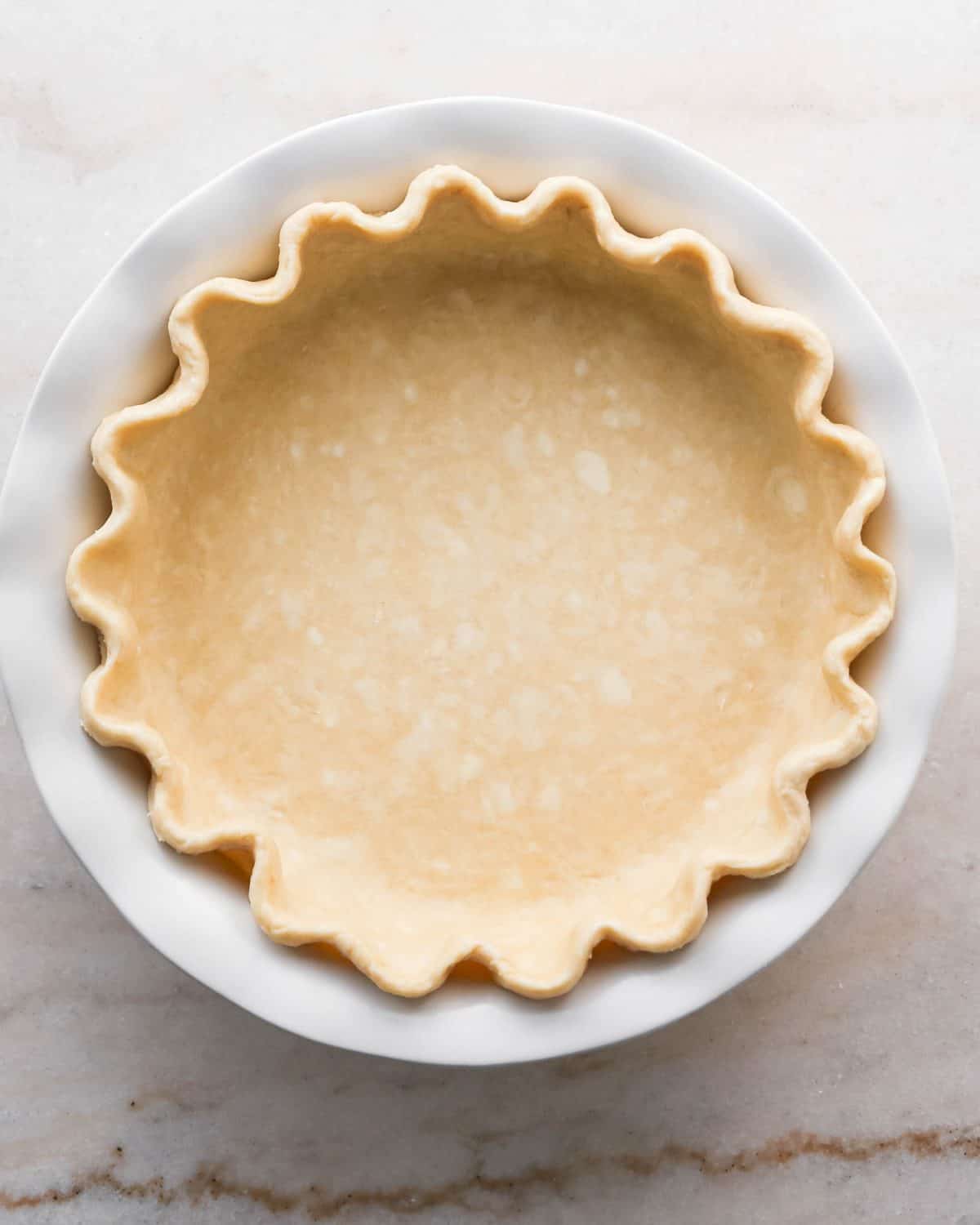 how to make pecan pie without corn syrup - pecan pie crust in the bottom of a white ceramic pie dish with a fluted edge
