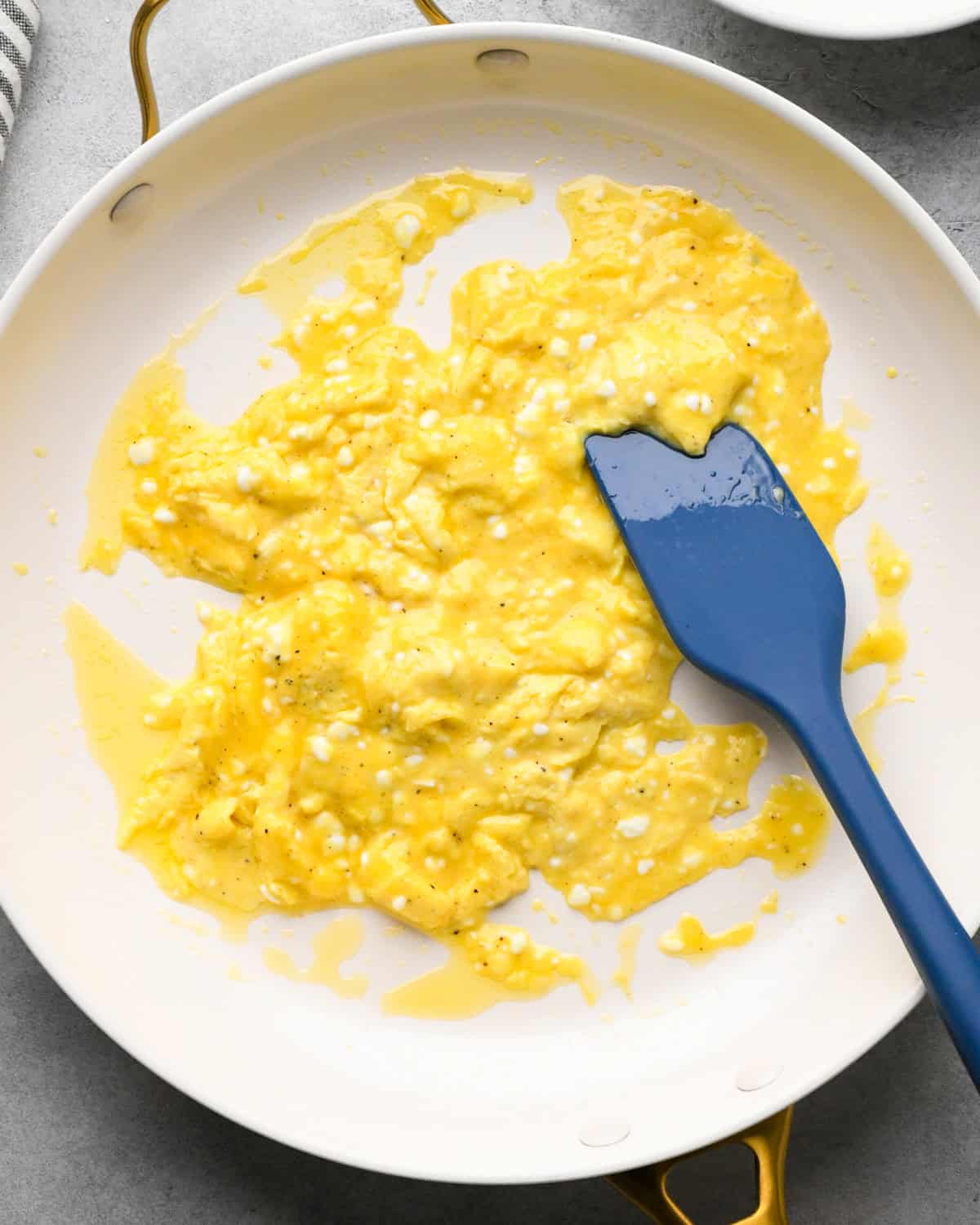 cottage cheese and eggs mixture in a white skillet while it's cooking and being stirred with a blue silicone spatula
