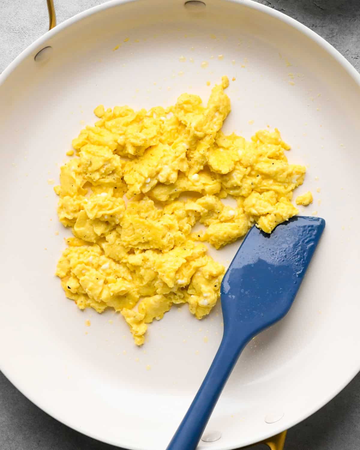 cottage cheese and scrambled eggs cooked in a white skillet with a blue silicone spatula