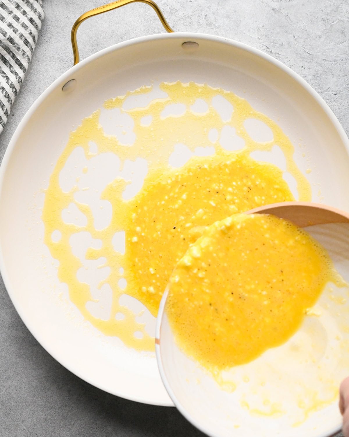 cottage cheese and eggs mixture being poured into a white skillet with melted butter