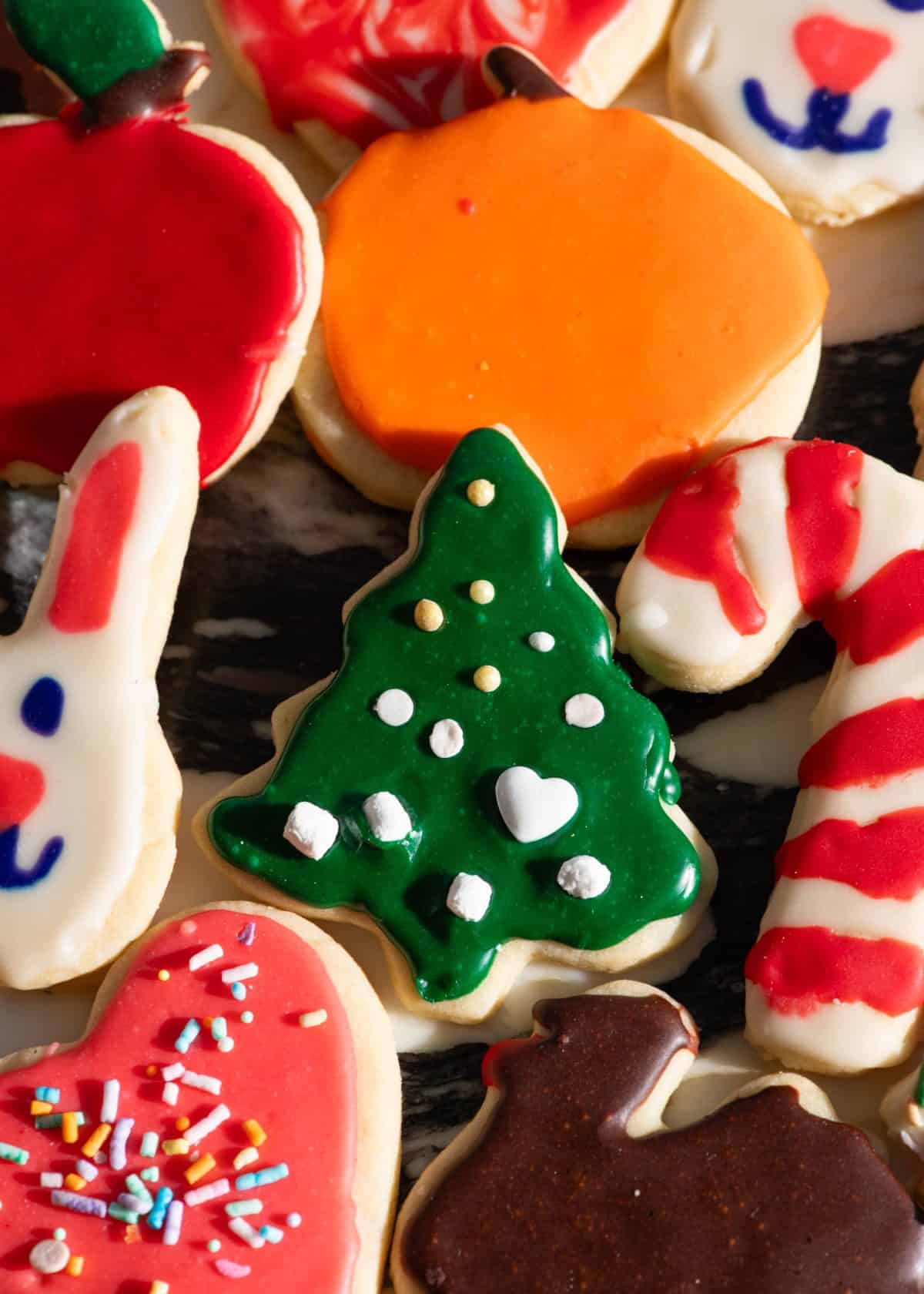 10 sugar cookies decorated with this sugar cookie icing recipe in the shapes of a christmas tree with green icing, a red and white candy cane, a white bunny, brown turkey, pink heart, orange pumpkin and red apple. 