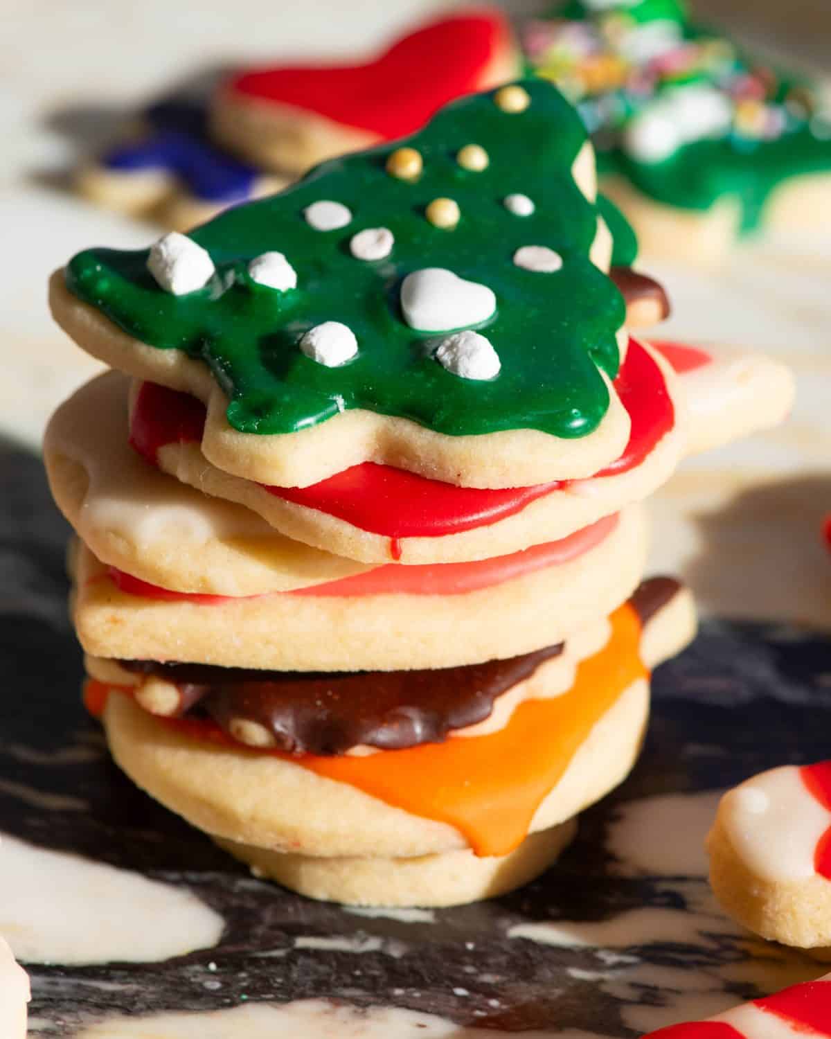 a stack of 7 sugar cookies decorated with this sugar cookie frosting recipe that is hardened and shiny, on top is a christmas tree with green icing and sprinkles, then under that is a red apple, then a white bunny, then a pink heart, then a brown turkey, then an orange pumpkin.