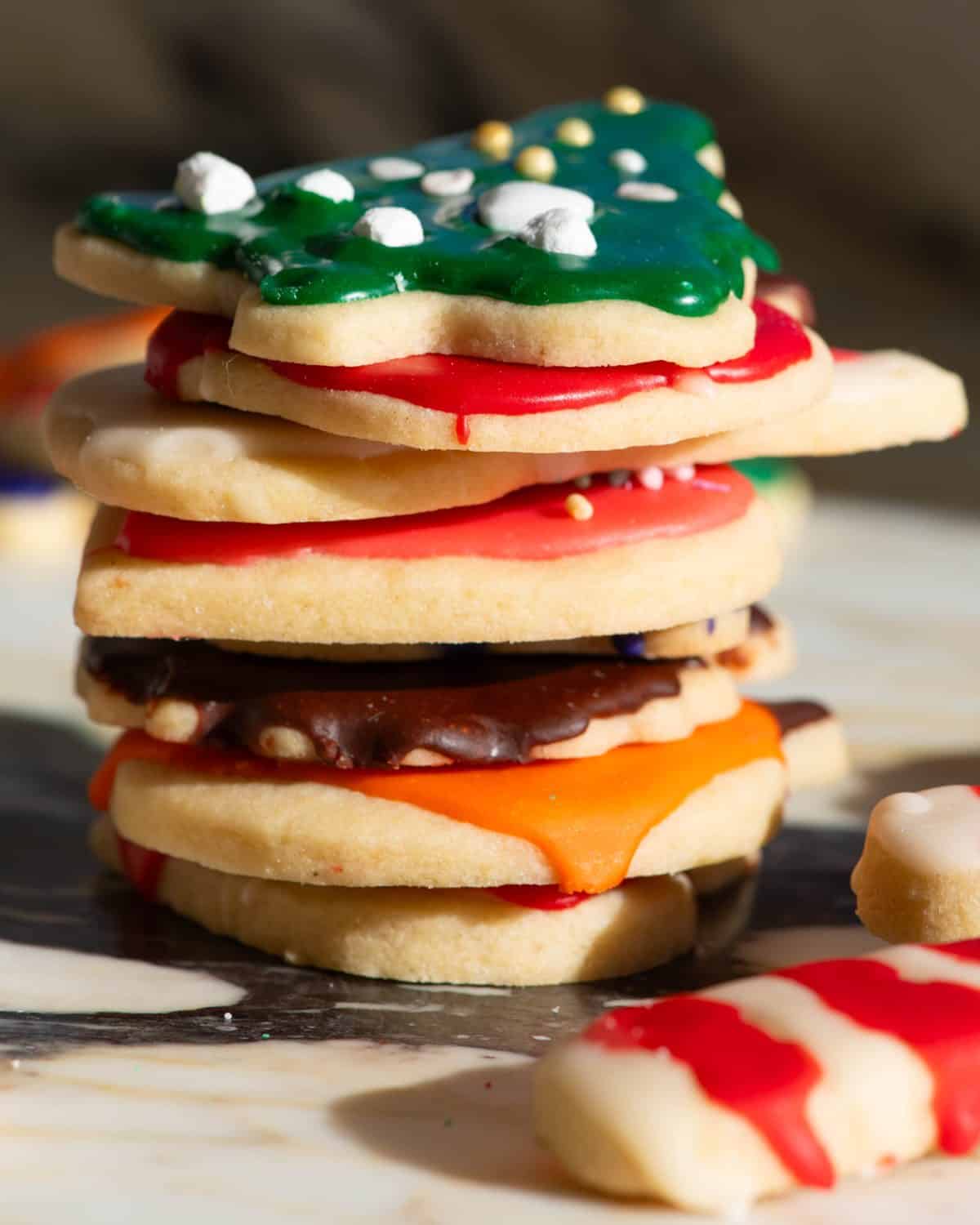 a stack of 8 sugar cookies decorated with this sugar cookie frosting recipe that is hardened and shiny, on top is a Christmas tree with green icing and sprinkles, then under that is a red apple, then a white bunny, then a pink heart, then a brown turkey, then an orange pumpkin.