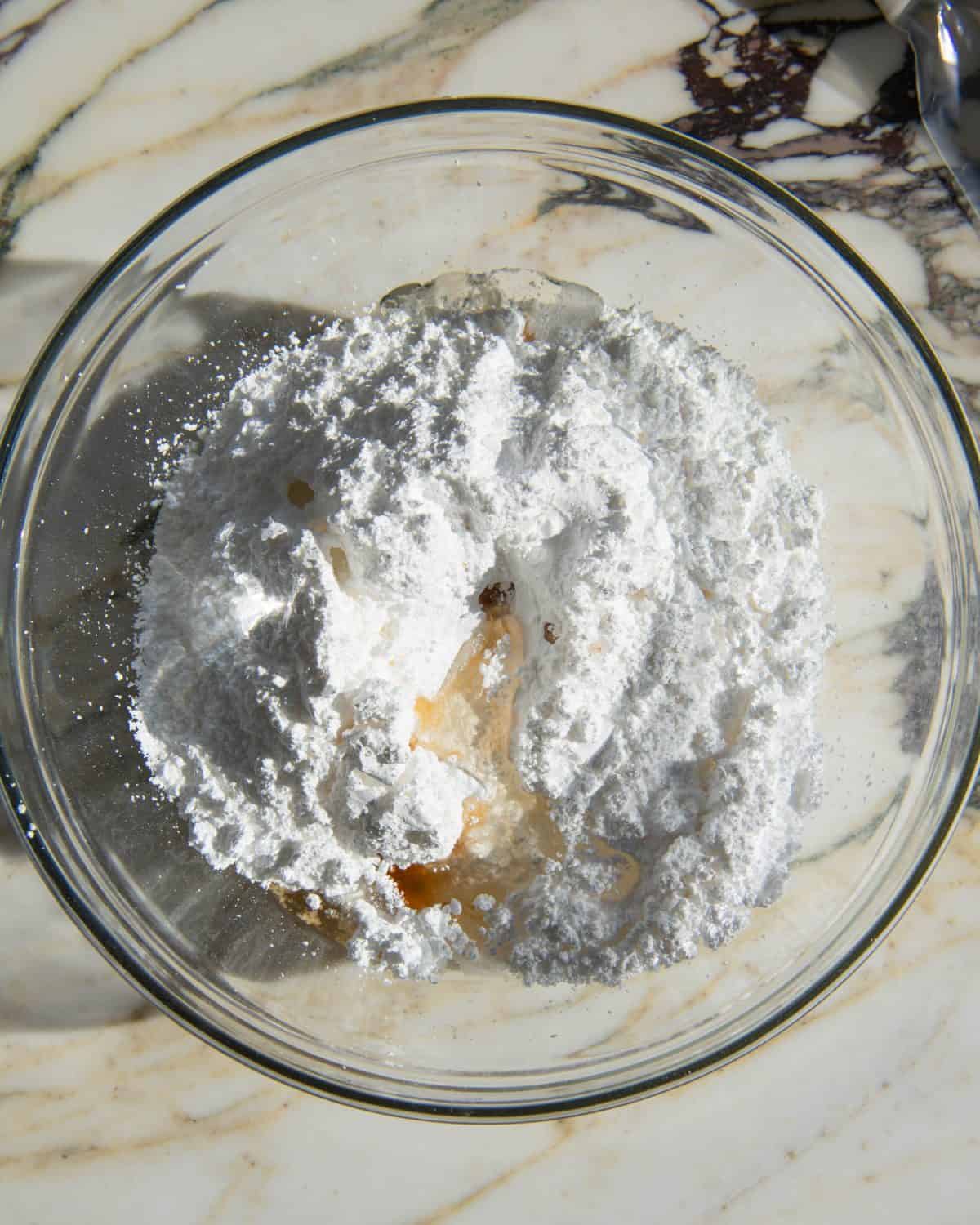 how to make sugar cookie icing - powdered sugar, milk, vanilla and corn syrup in a glass bowl on a white surface