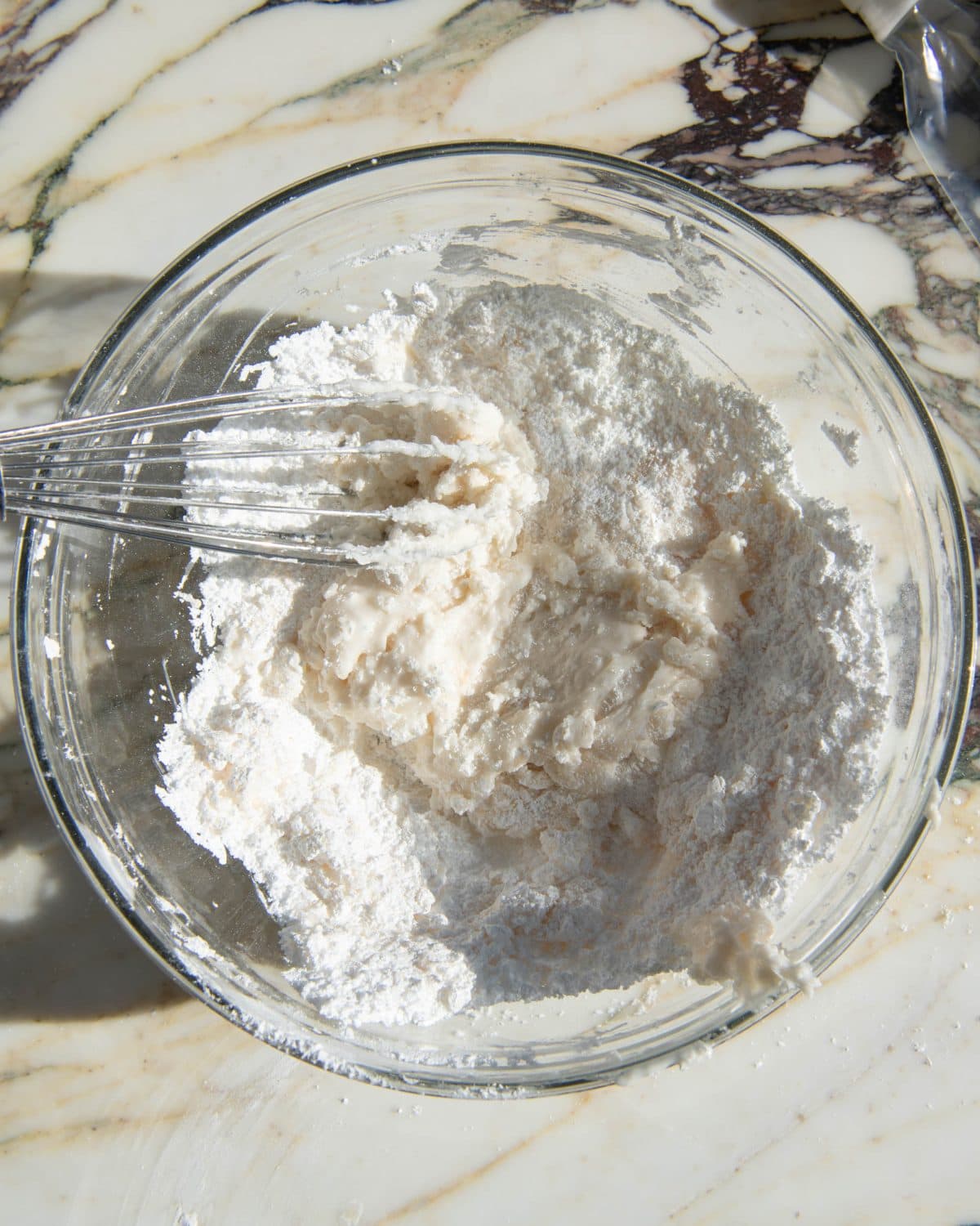 how to make sugar cookie icing - ingredients in a glass bowl on a marble surface being whisked with a metal whisk