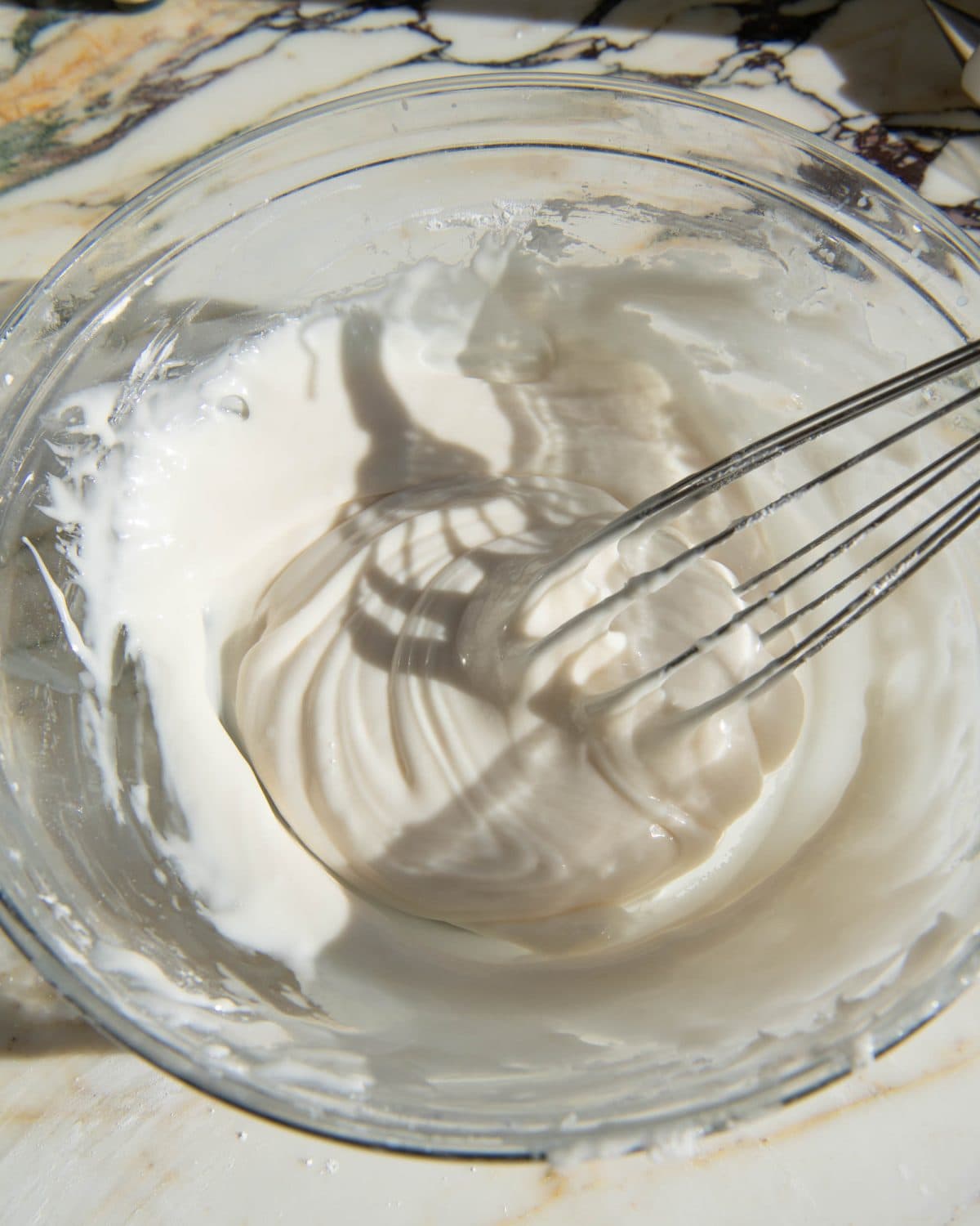 sugar cookie icing in a glass bowl on a marble surface being whisked with a metal whisk