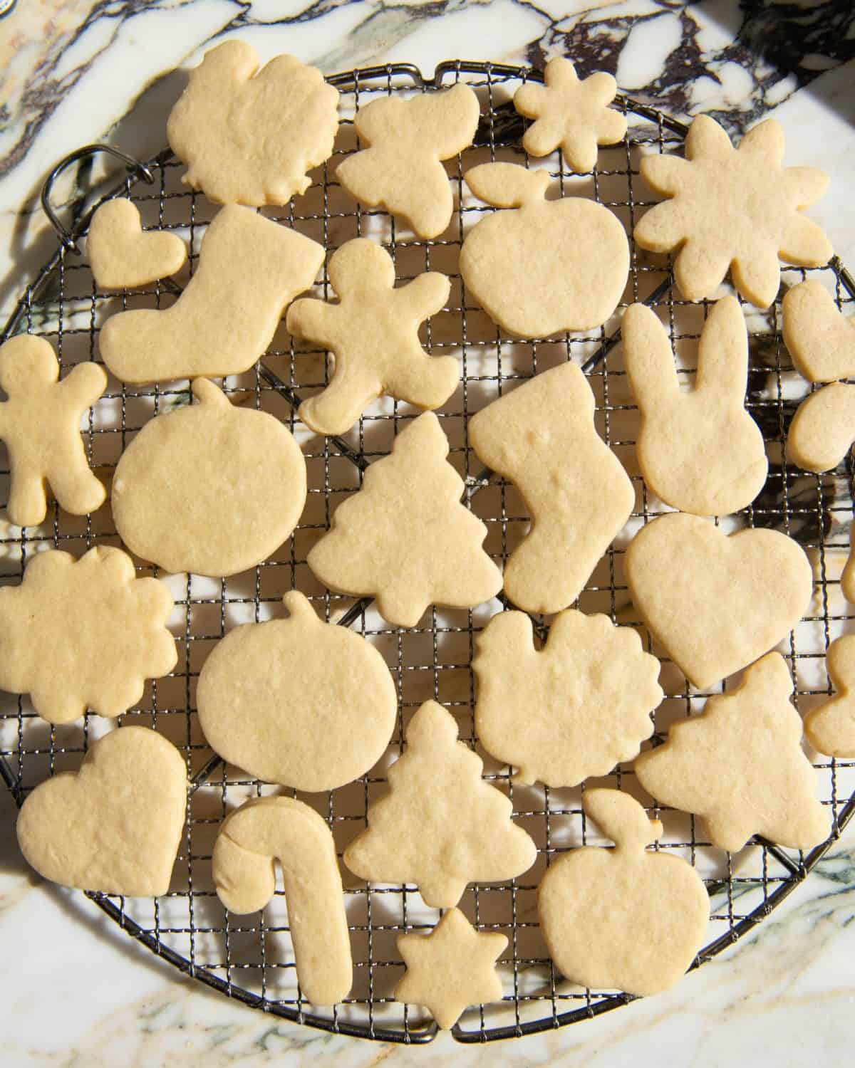 baked cut out sugar cookies on a round metal wire cooling rack in the shapes of Christmas trees, pumpkins, turkeys, hearts, bunnies, gingerbread men, flowers, candy canes, stars and apples