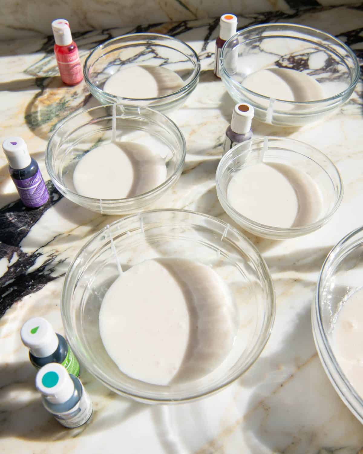 white sugar cookie icing in 6 bowls, with a bottle of gel food coloring next to each bowl